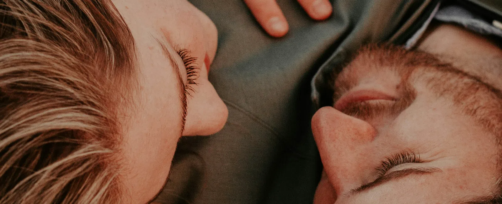 Close-up of a couple lying close with eyes closed, showing intimacy and tender connection.